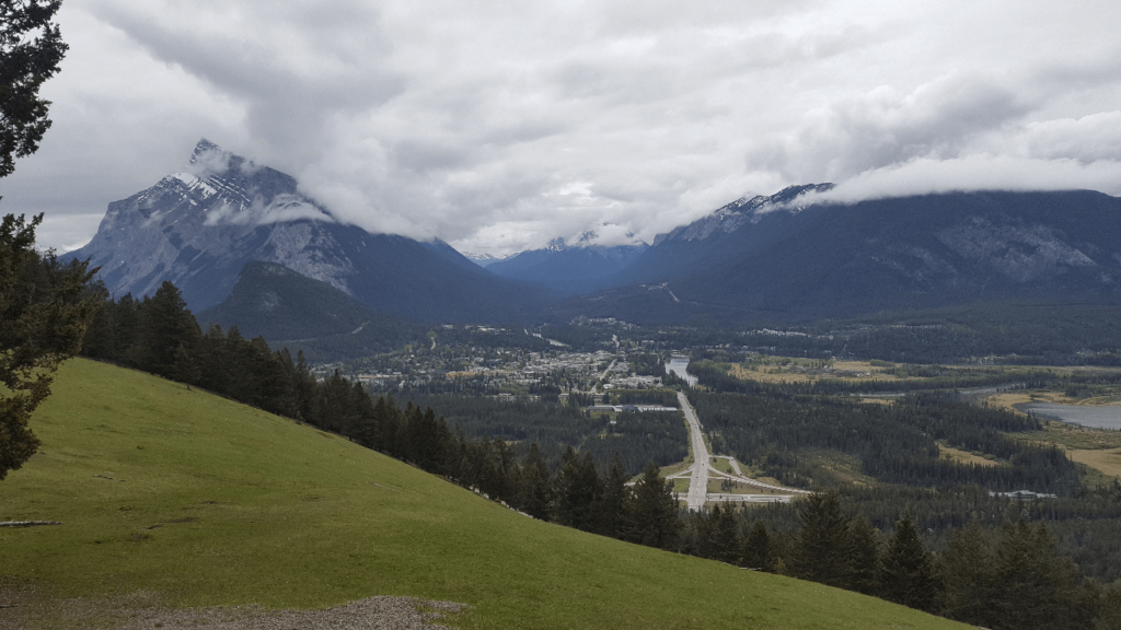 Mount Norquay Lookout, looking over the town of Banff. Steep mountains shrouded with clouds and a forested city below