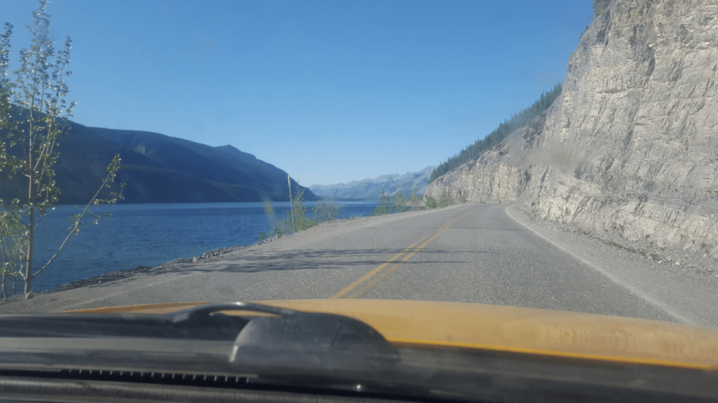 driving along a lake, with a vertical cliff on the right and a cliff off into the lake on the left