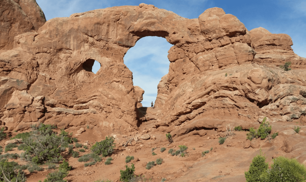 standing in the middle of a very tall red rock arch