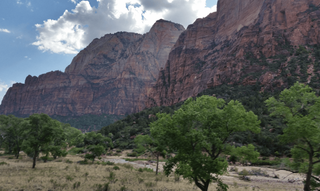 gigantic red rock cliffs with green trees at bottom