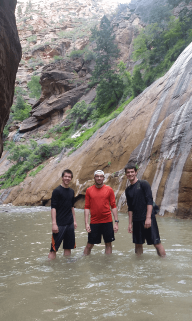 three amigos standing in a river in a tall and wide slot canyon