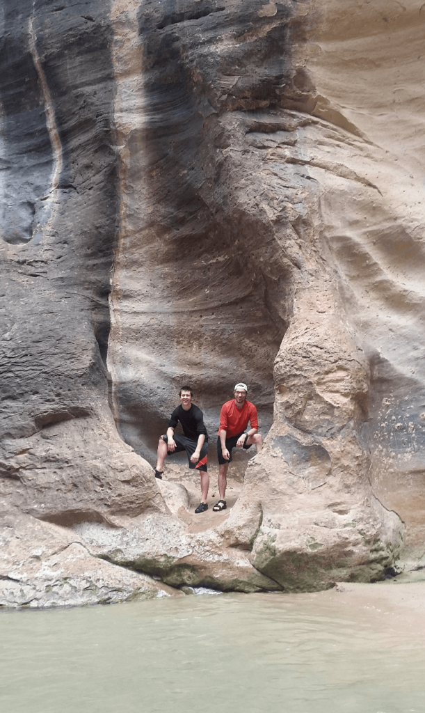 mike and joseph in an alcove in a sandstone cliff with the virgin river below
