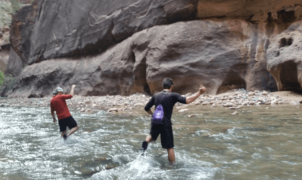 robert and mike splashing across a river with sandstone cliffs behind
