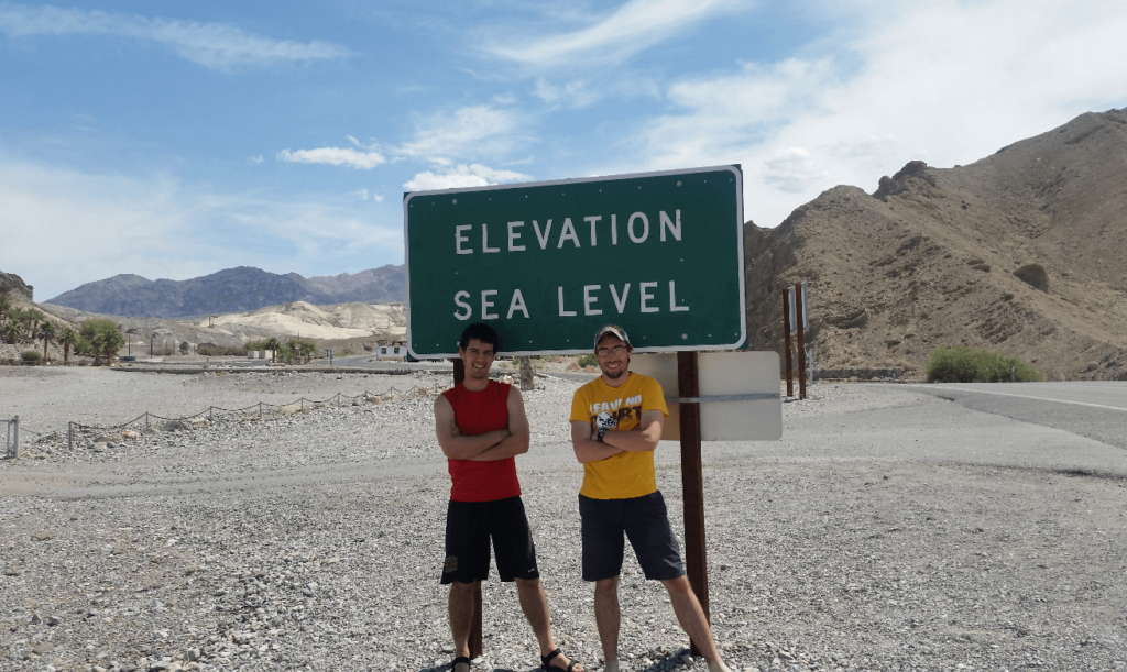 robert and mike at a green highway sign that says "elevation sea level"