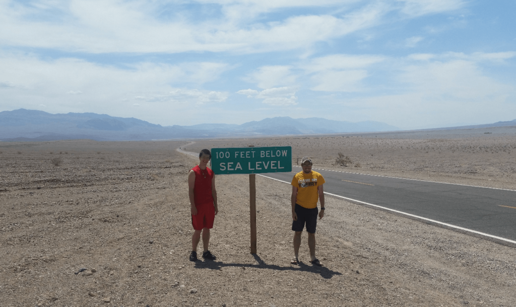 joseph and mike at a green highway sign that says "100 feet below sea level"