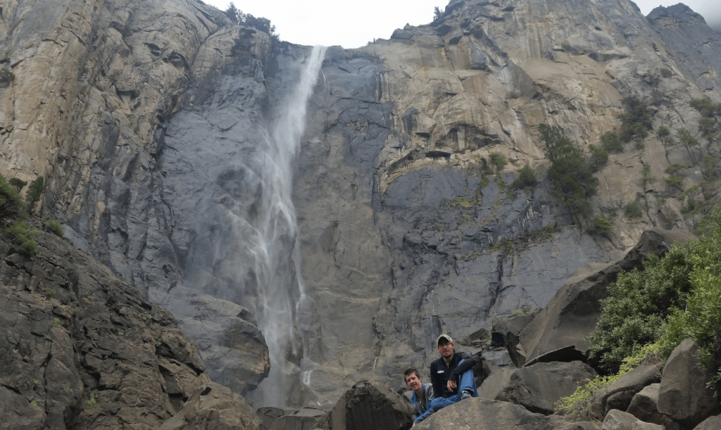 mike and joseph in front of Bridalveil Falls in Yosemite- A super tall waterfall with low flow that rarely allows the water to get to the bottom without turning to mist