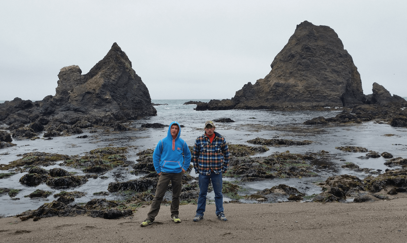 mike and joseph with warm clothes on in front of a frothy sea