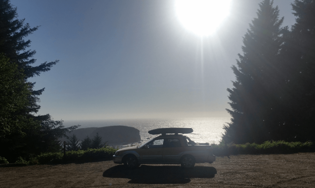 subaru baja parking overlooking the pacific ocean with pine trees on either side