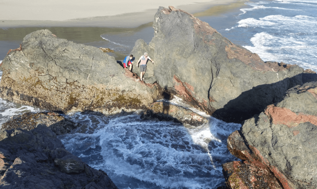 mike and joseph clambering around on rocks with waves crashing in between