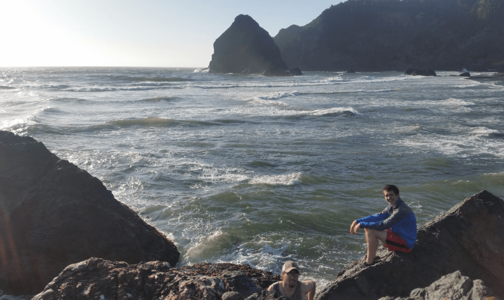 joseph and mike sitting on rocks next to the ocean with waves crashing in