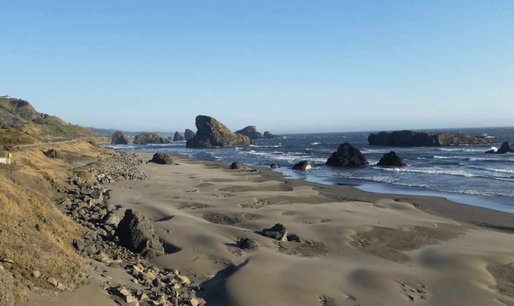 highway next to a sandy beach next to the ocean with huge seamounts sticking out of the water