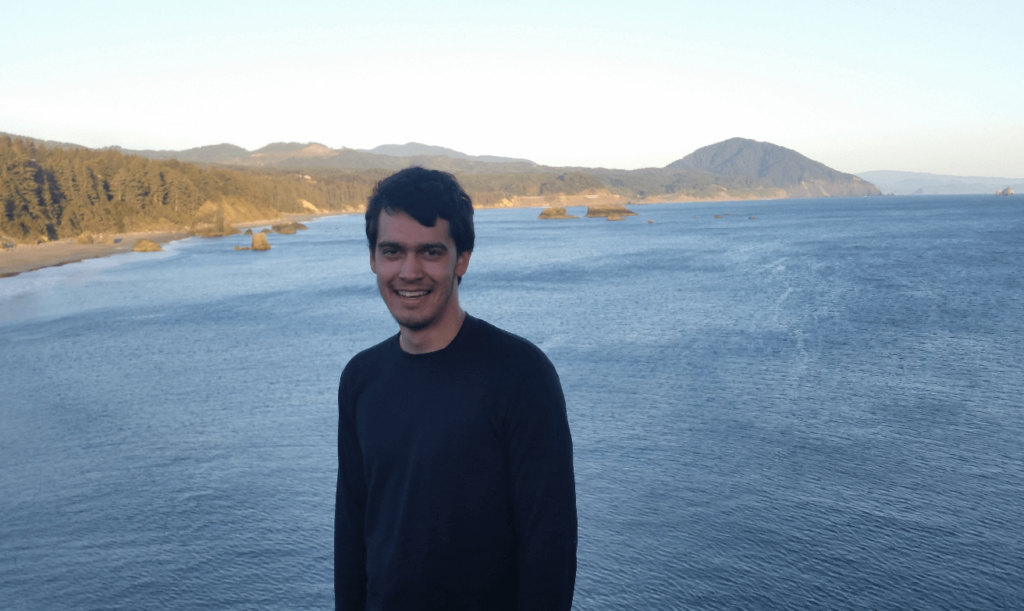 Robert standing in front on a pine forest on the shore of the ocean