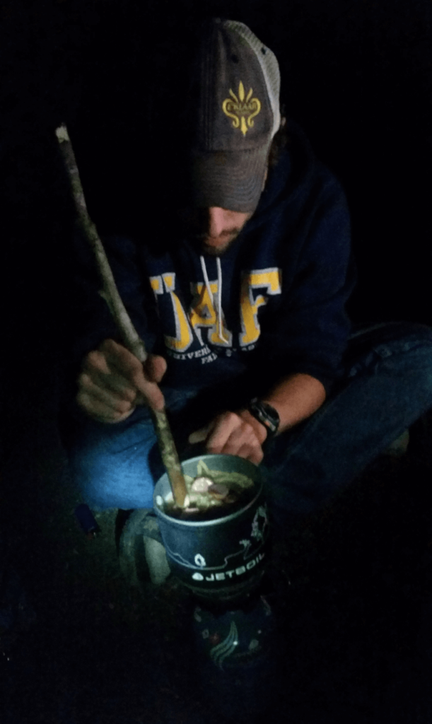 mike illuminated by a headlamp stirring mac n cheese in a jetboil with a stick