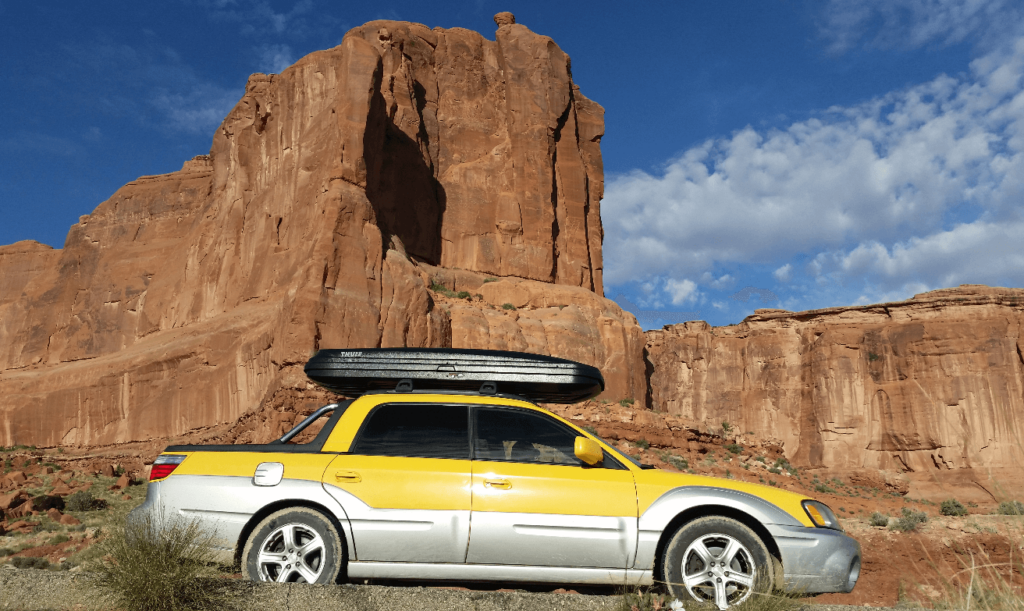 subaru baja in front of red rock cliff in arches national park